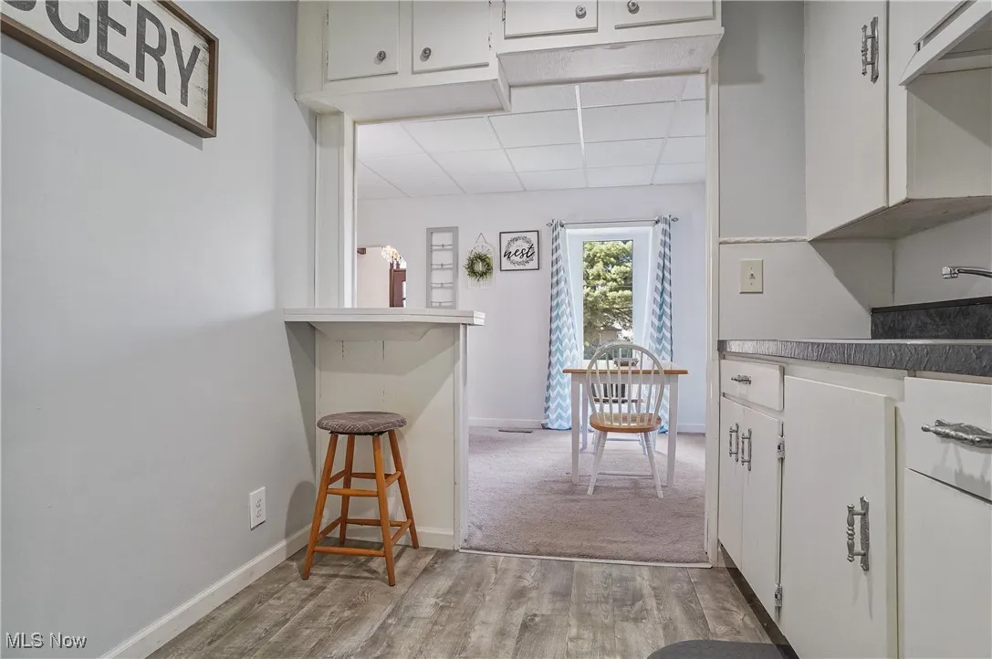 Kitchen featuring a breakfast bar, light wood-type flooring, white cabinets, and a paneled ceiling
