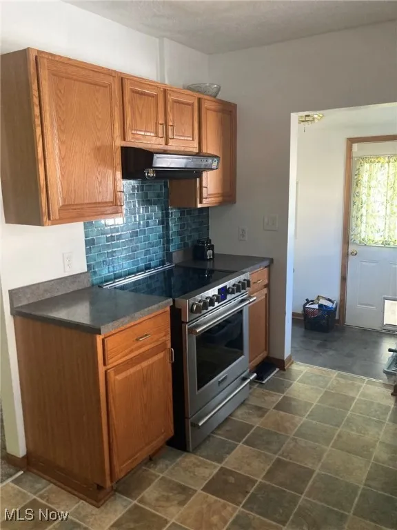 Kitchen featuring electric range, dark countertops, brown cabinetry, and tasteful backsplash