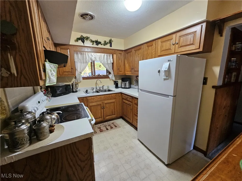 Kitchen with brown cabinetry, light flooring, white appliances, light countertops, and a textured ceiling