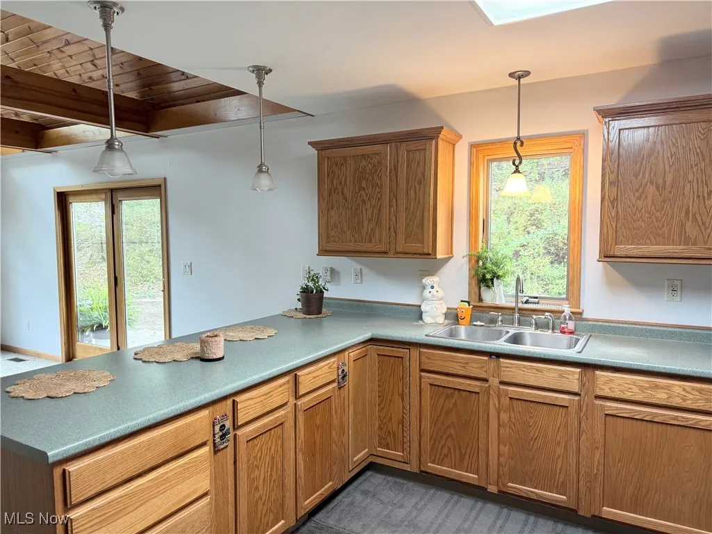 Kitchen featuring a peninsula, hanging light fixtures, a skylight, brown cabinetry, and wooden ceiling