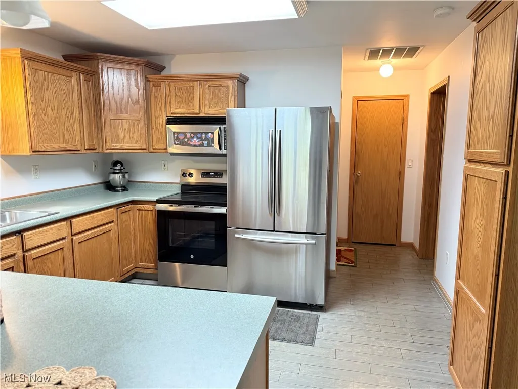 Kitchen featuring appliances with stainless steel finishes, light countertops, light wood finished floors, and brown cabinetry