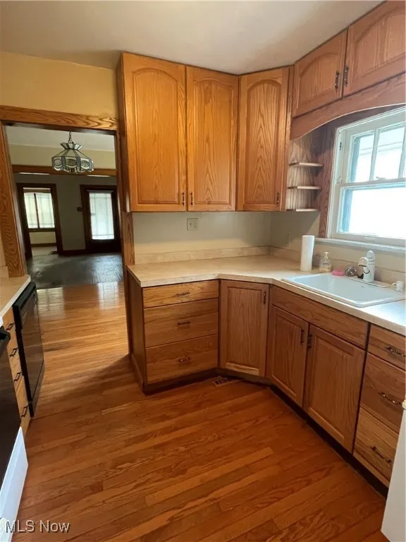 Kitchen featuring healthy amount of natural light, dark wood-type flooring, light countertops, and brown cabinets
