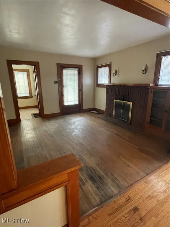 Unfurnished living room featuring hardwood / wood-style flooring, healthy amount of natural light, and a brick fireplace