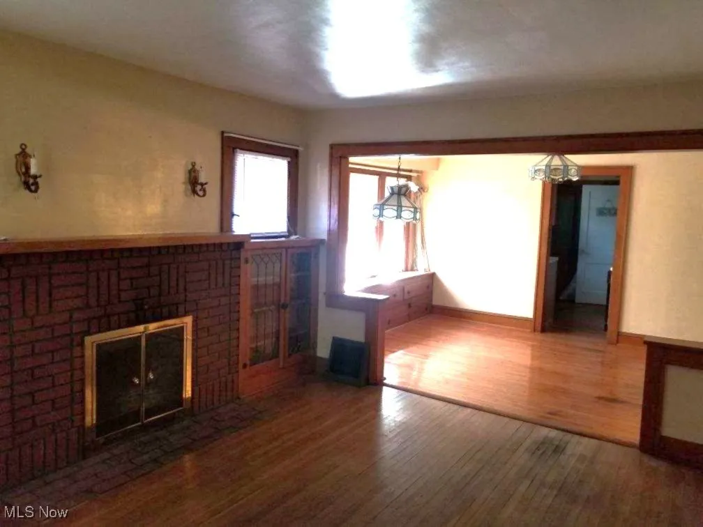 Unfurnished living room featuring wood finished floors and a brick fireplace
