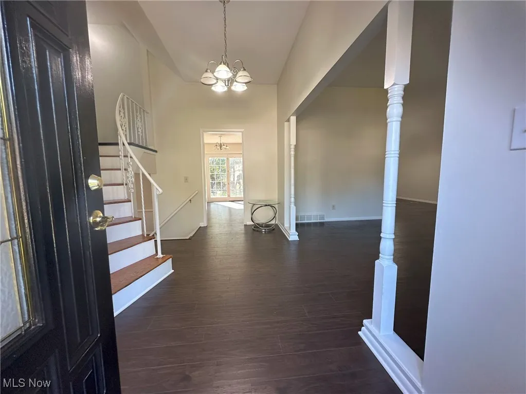 Foyer with dark wood-style flooring, stairway, a chandelier, and a high ceiling