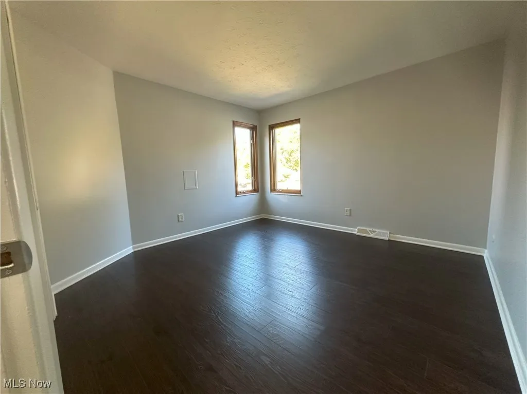 Spare room featuring dark wood-type flooring and baseboards