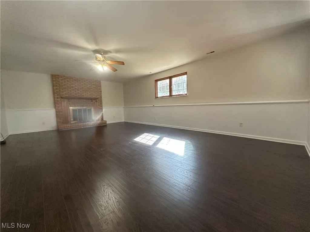 Unfurnished living room with dark wood finished floors, a ceiling fan, and a brick fireplace