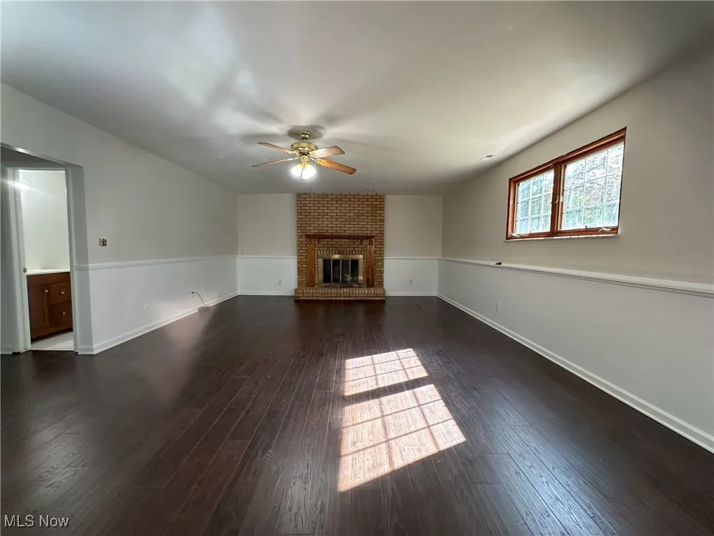 Unfurnished living room with a ceiling fan, dark wood finished floors, and a brick fireplace