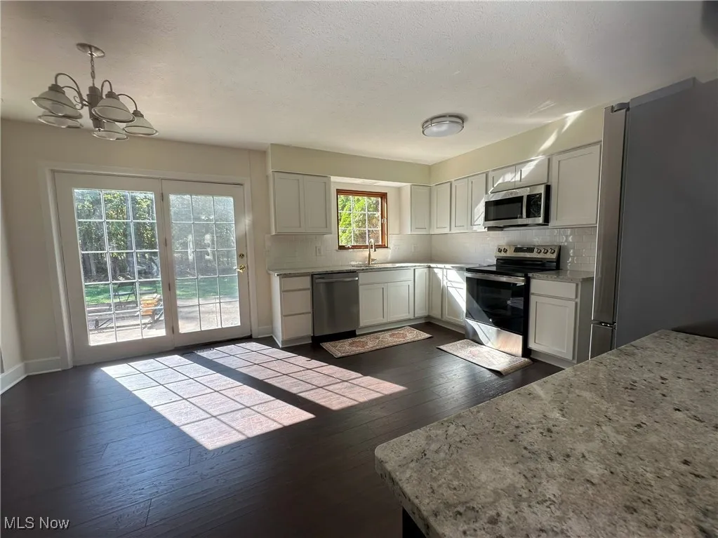 Kitchen with appliances with stainless steel finishes, backsplash, white cabinetry, light stone countertops, and a textured ceiling