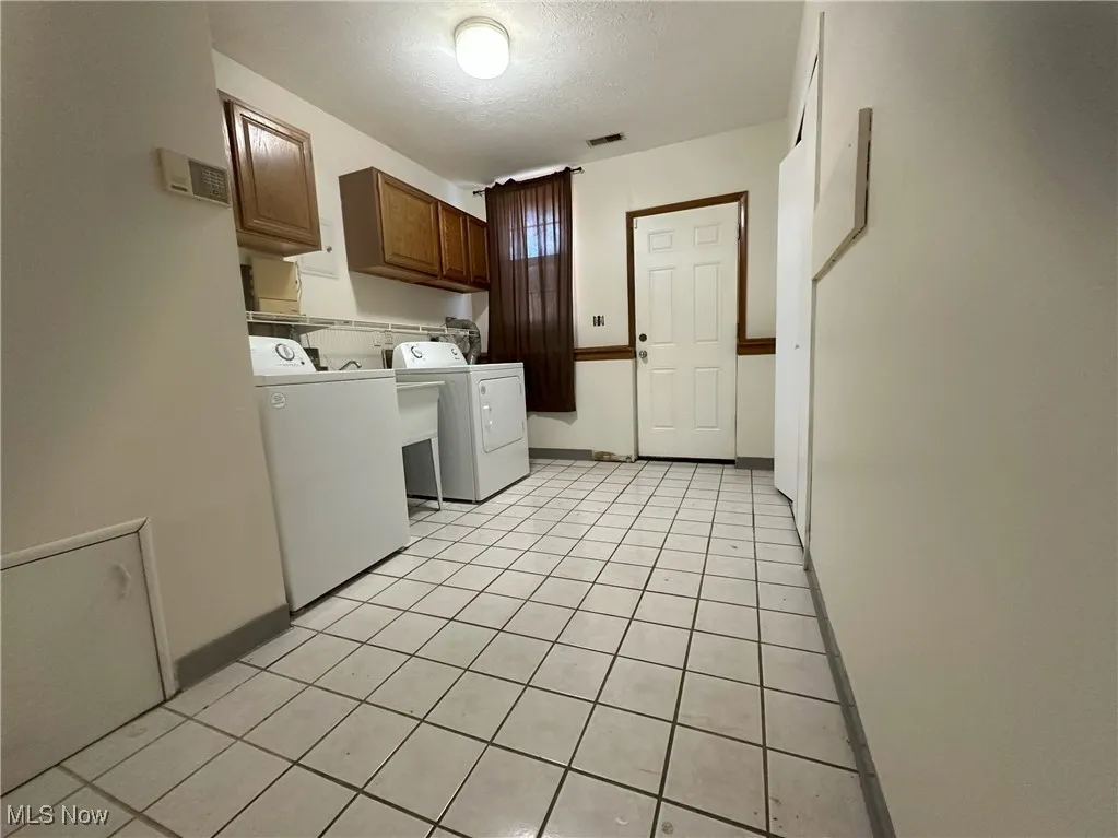 Washroom with cabinet space, light tile patterned floors, washer and dryer, and a textured ceiling