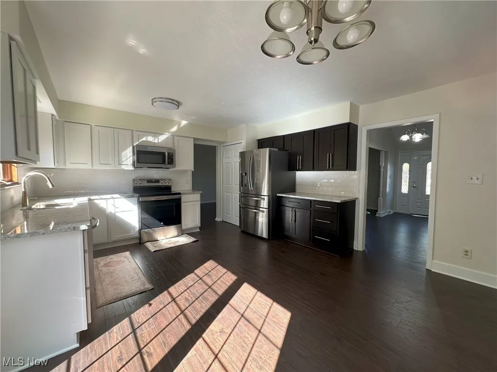 Kitchen featuring a chandelier, decorative backsplash, stainless steel appliances, light stone counters, and dark wood-type flooring