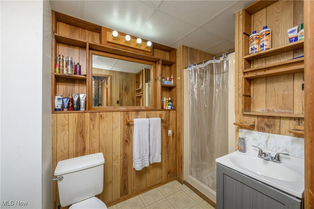 Bathroom with wood walls, vanity, a drop ceiling, and a shower stall
