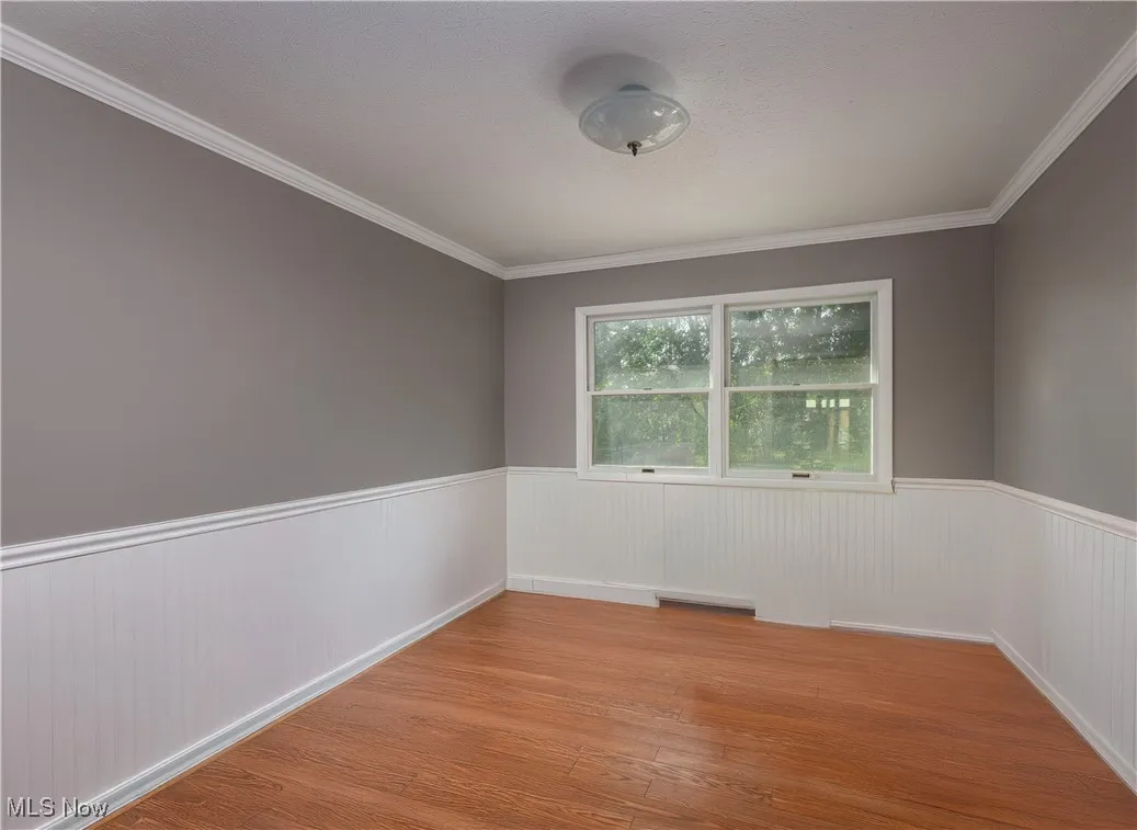 Unfurnished room with light wood-type flooring, crown molding, and wainscoting