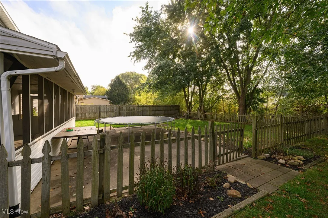 Fenced backyard with a trampoline, a sunroom, and a patio area