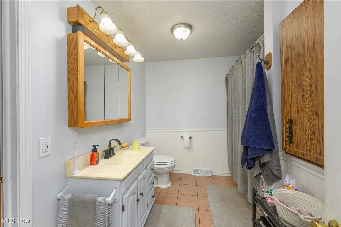 Full bath with wainscoting, a textured ceiling, vanity, light tile patterned floors, and curtained shower