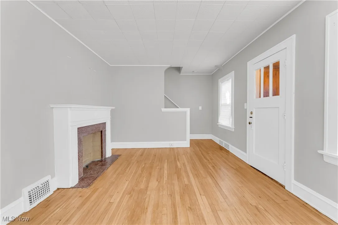Entryway with light wood finished floors, crown molding, and a fireplace with flush hearth