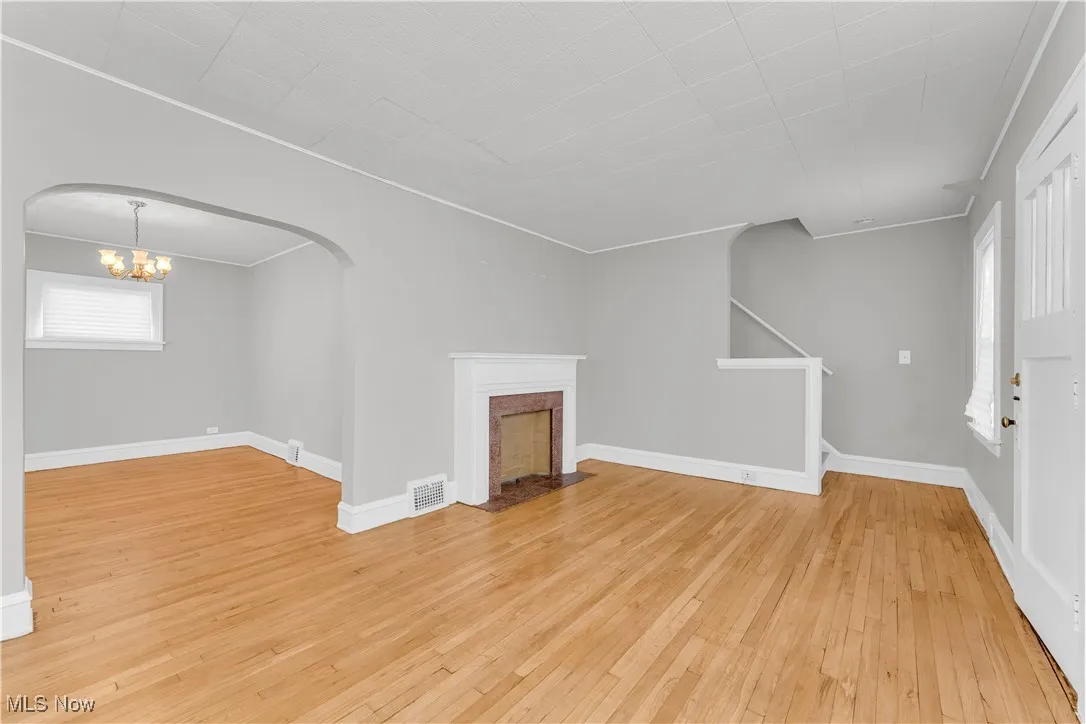Unfurnished living room with a fireplace with flush hearth, light wood-style flooring, a chandelier, arched walkways, and ornamental molding