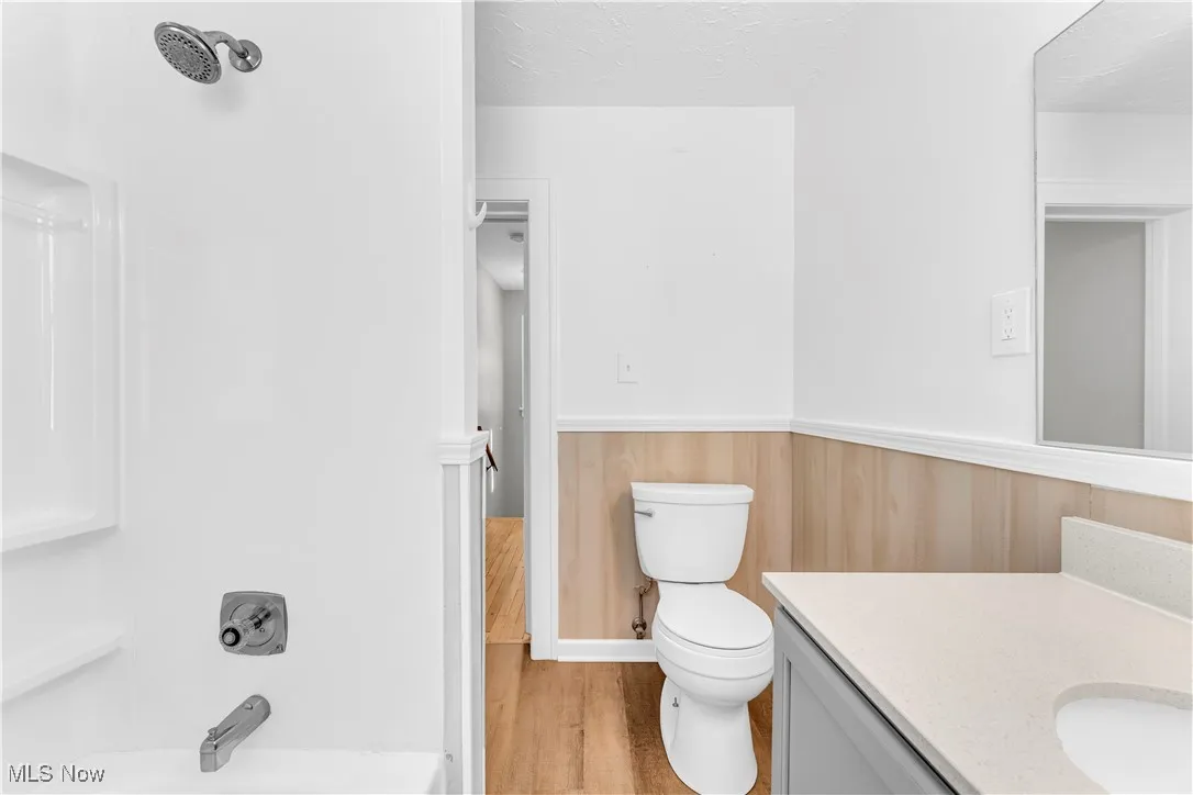 Bathroom featuring bathtub / shower combination, light wood-style floors, vanity, a textured ceiling, and a wainscoted wall