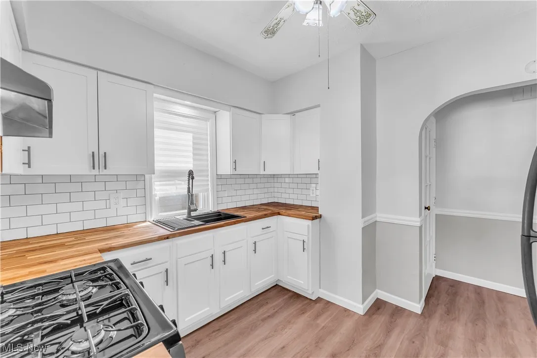 Kitchen with butcher block countertops, light wood-style flooring, white cabinetry, and tasteful backsplash