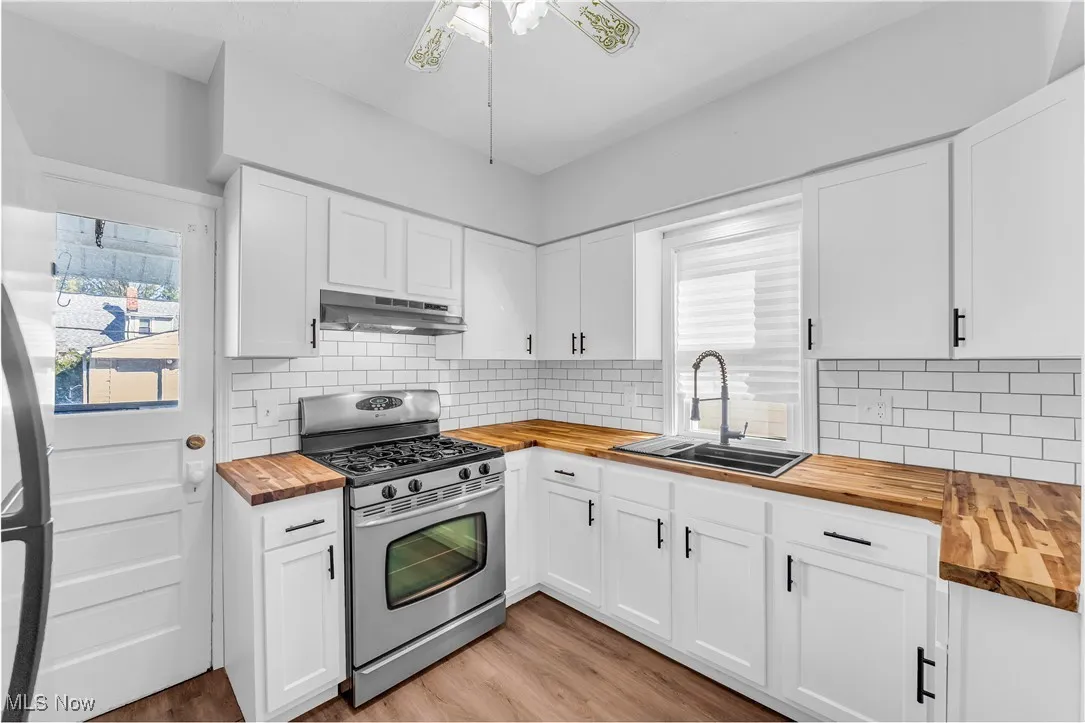 Kitchen with butcher block countertops, stainless steel gas stove, and white cabinetry