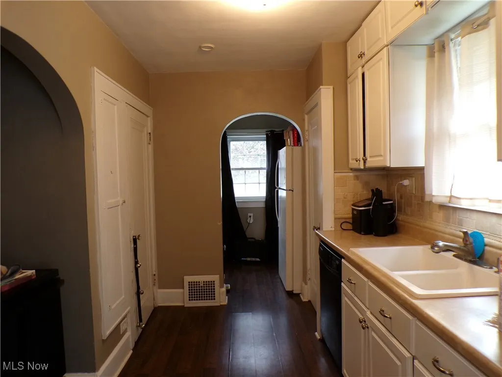 Kitchen with white cabinetry, arched walkways, light countertops, dark wood-style flooring, and decorative backsplash
