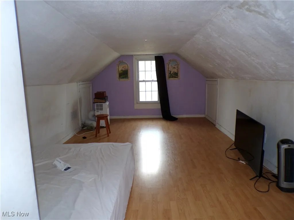 Additional living space (upper bedroom #3) featuring light wood-style flooring, vaulted ceiling, and a textured ceiling