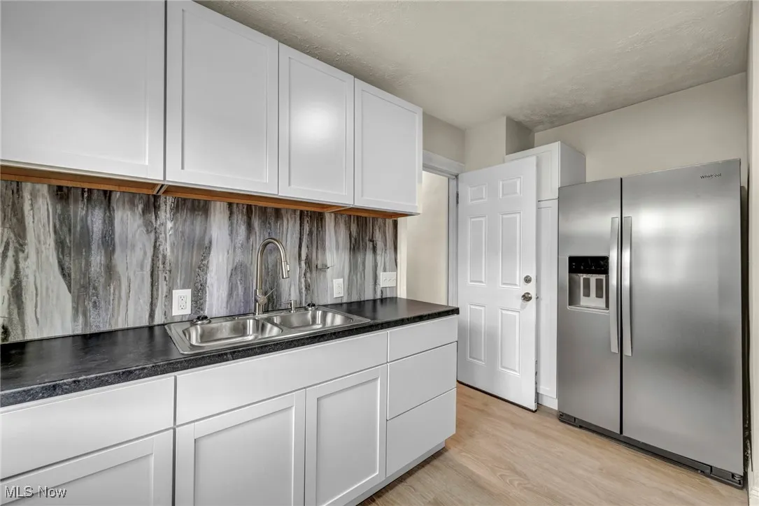 Kitchen with stainless steel refrigerator with ice dispenser, light wood-style flooring, white cabinetry, and dark countertops