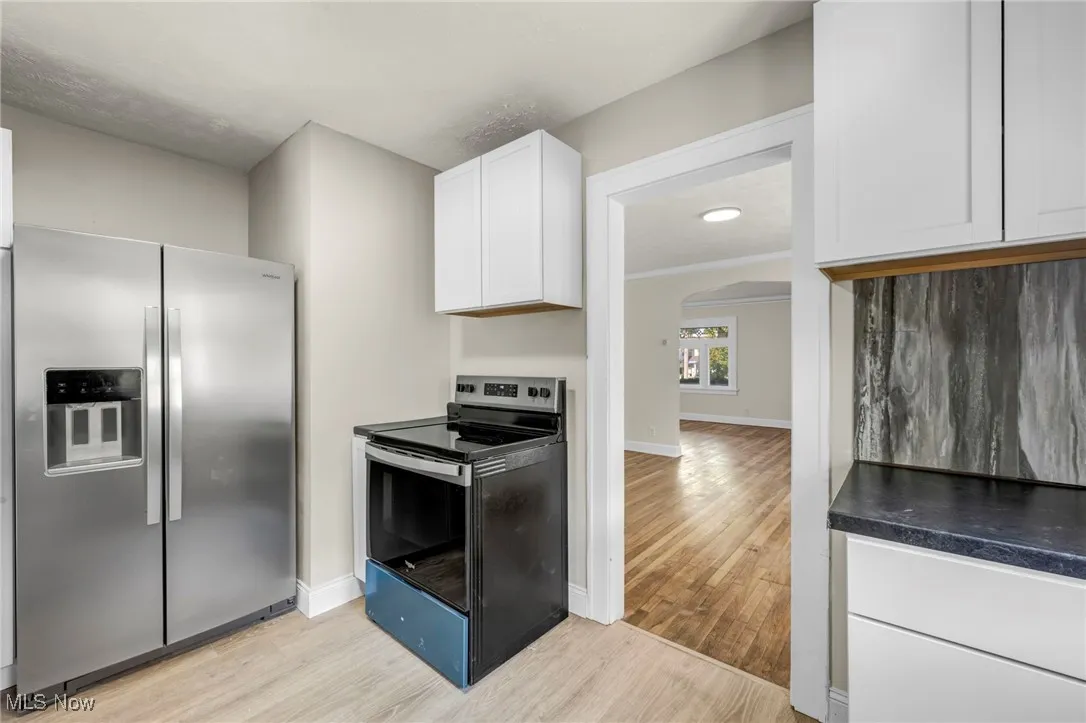 Kitchen with stainless steel appliances, white cabinetry, arched walkways, light wood-style flooring, and dark countertops