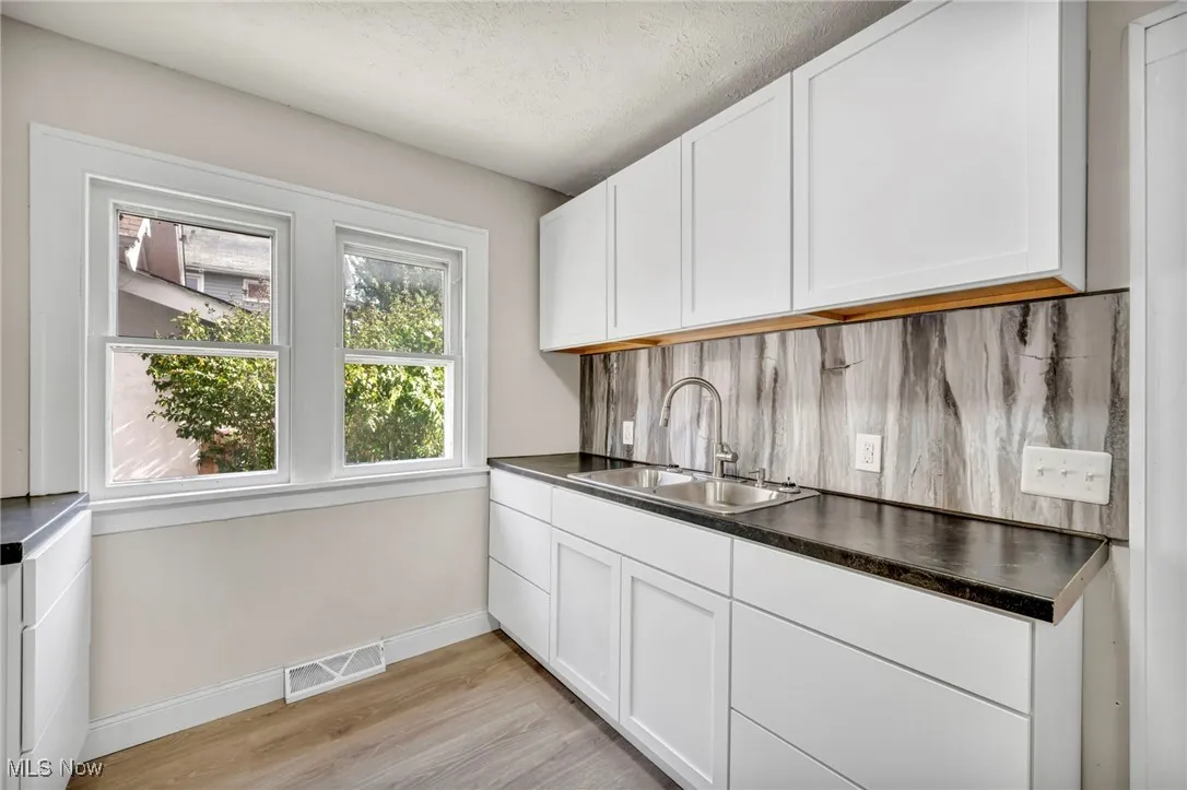 Kitchen with white cabinets, backsplash, a textured ceiling, light wood-type flooring, and dark countertops