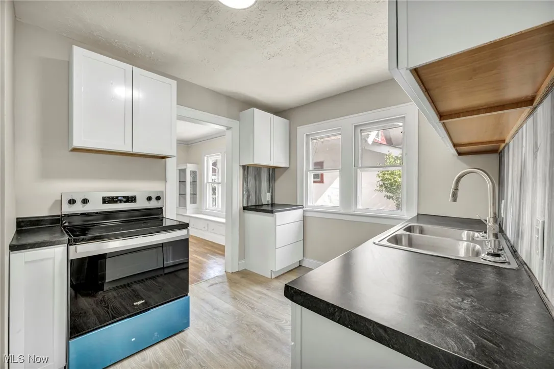 Kitchen with stainless steel range with electric cooktop, white cabinets, light wood-type flooring, dark countertops, and a textured ceiling