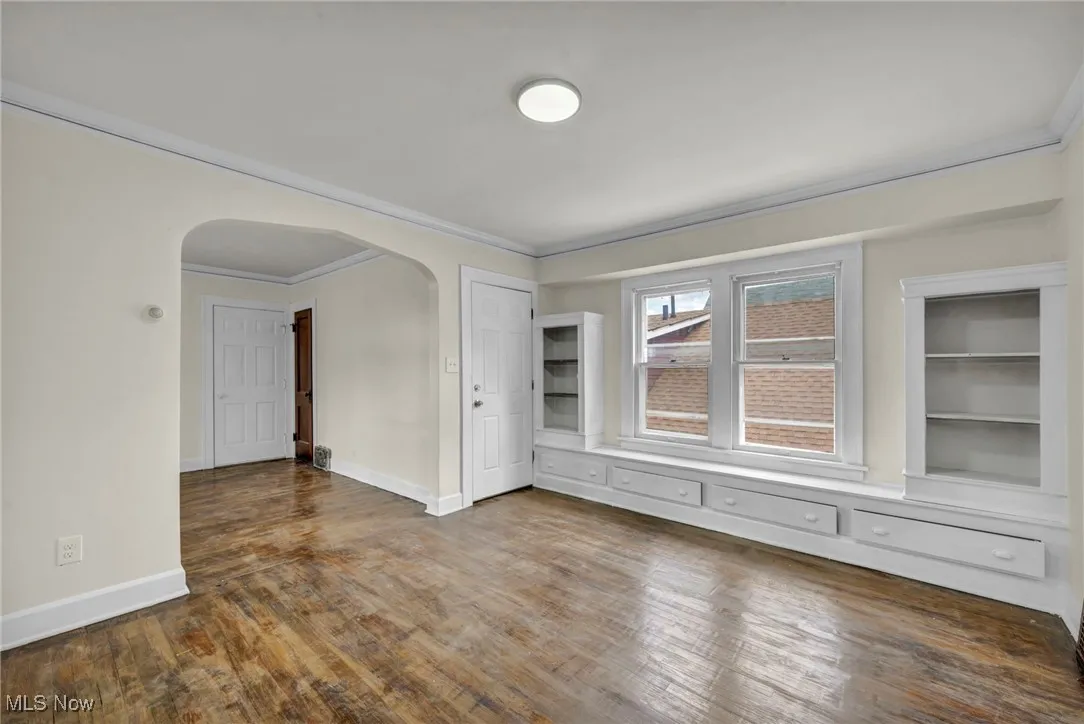 Empty room with arched walkways, ornamental molding, and dark wood-type flooring