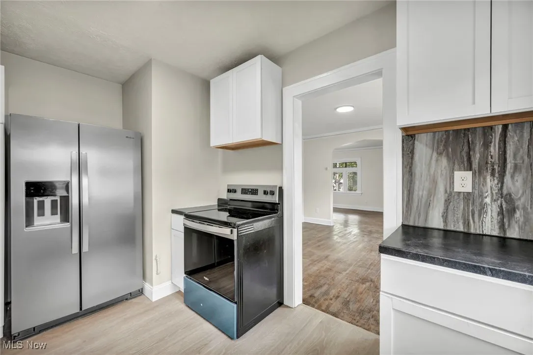 Kitchen with appliances with stainless steel finishes, dark countertops, white cabinetry, and light wood-style floors