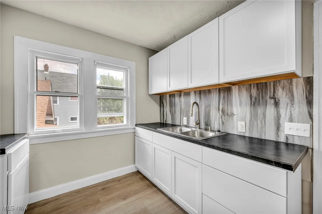 Kitchen featuring tasteful backsplash, white cabinetry, light wood-style flooring, dark countertops, and a textured ceiling