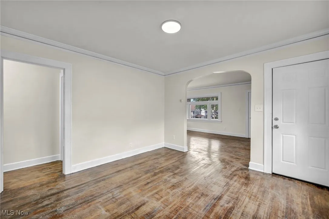 Unfurnished room featuring arched walkways, dark wood finished floors, and crown molding