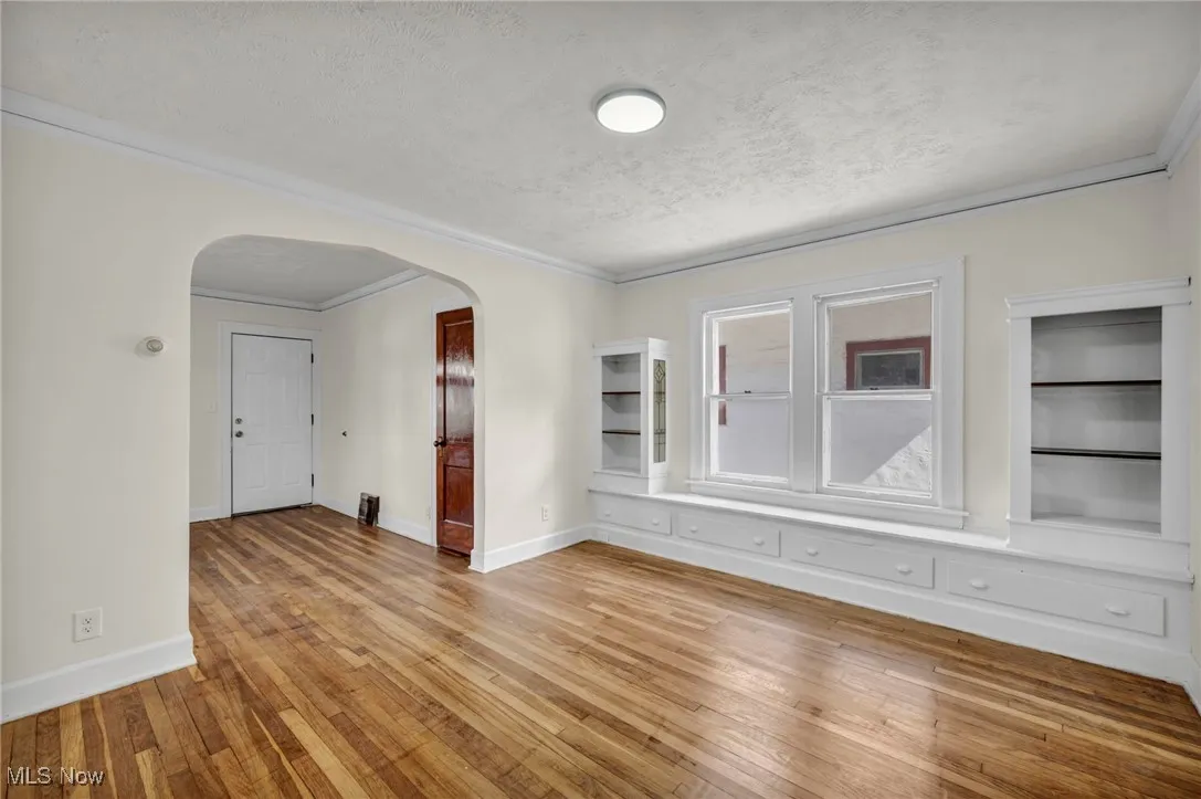 Empty room with ornamental molding, light wood-type flooring, a textured ceiling, and arched walkways