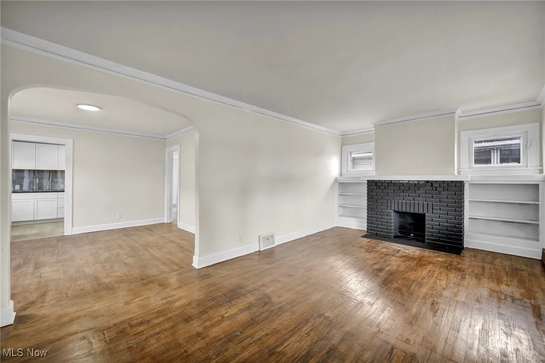 Unfurnished living room with arched walkways, a brick fireplace, hardwood / wood-style flooring, and ornamental molding
