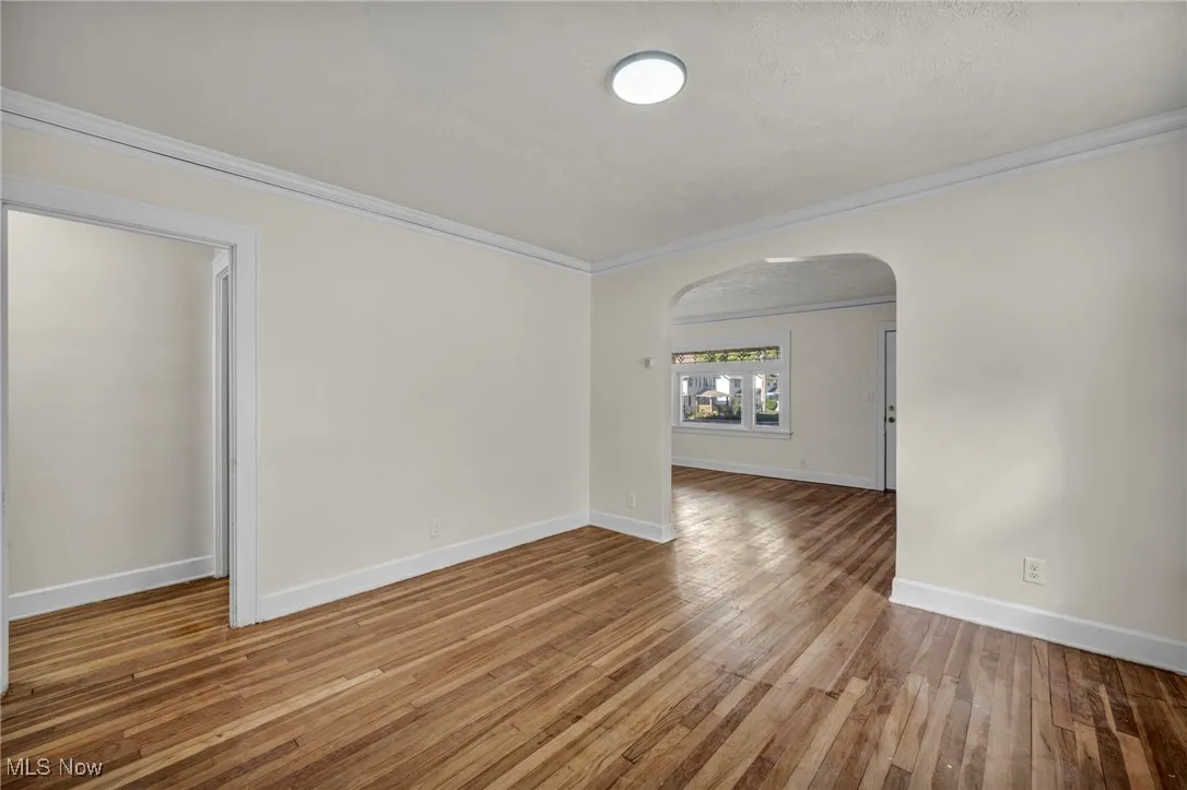 Empty room with ornamental molding, arched walkways, and light wood-style floors