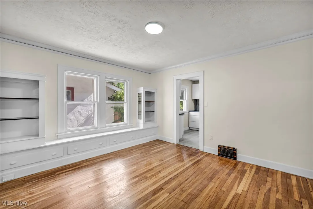 Spare room featuring light wood-type flooring, a textured ceiling, and ornamental molding
