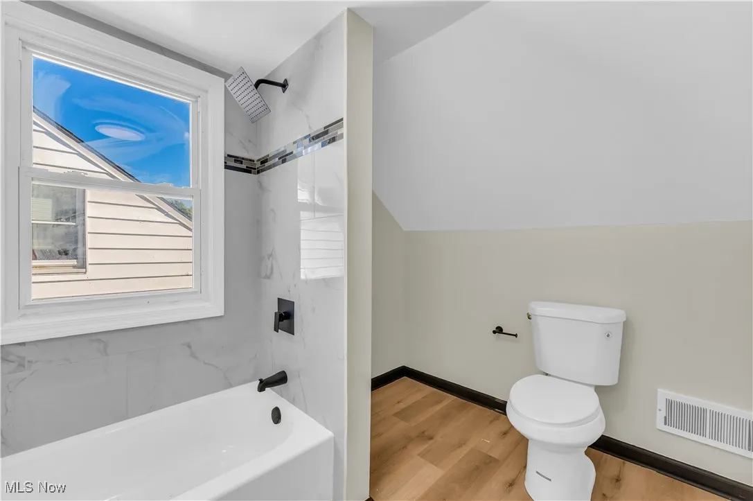 Bathroom featuring shower / bath combination, wood finished floors, and lofted ceiling