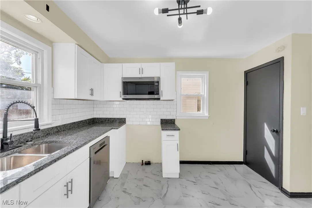 Kitchen with backsplash, white cabinetry, appliances with stainless steel finishes, light marble finish flooring, and dark stone counters