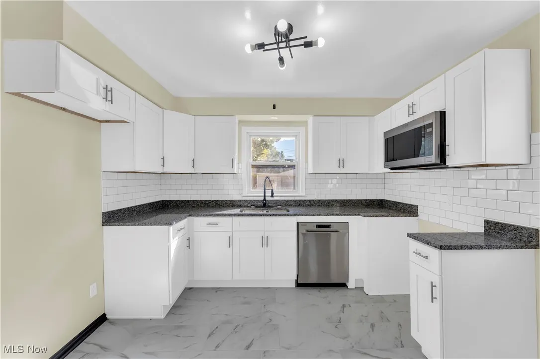 Kitchen with dark stone countertops, stainless steel appliances, white cabinets, and backsplash