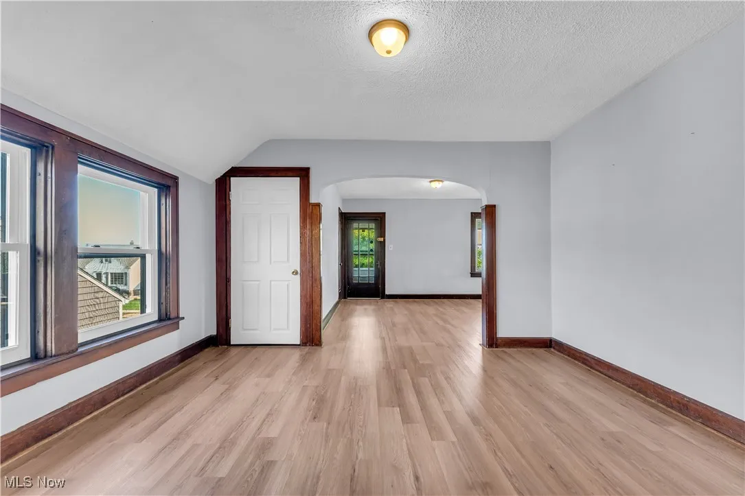 Spare room with arched walkways, light wood-style flooring, a textured ceiling, and vaulted ceiling
