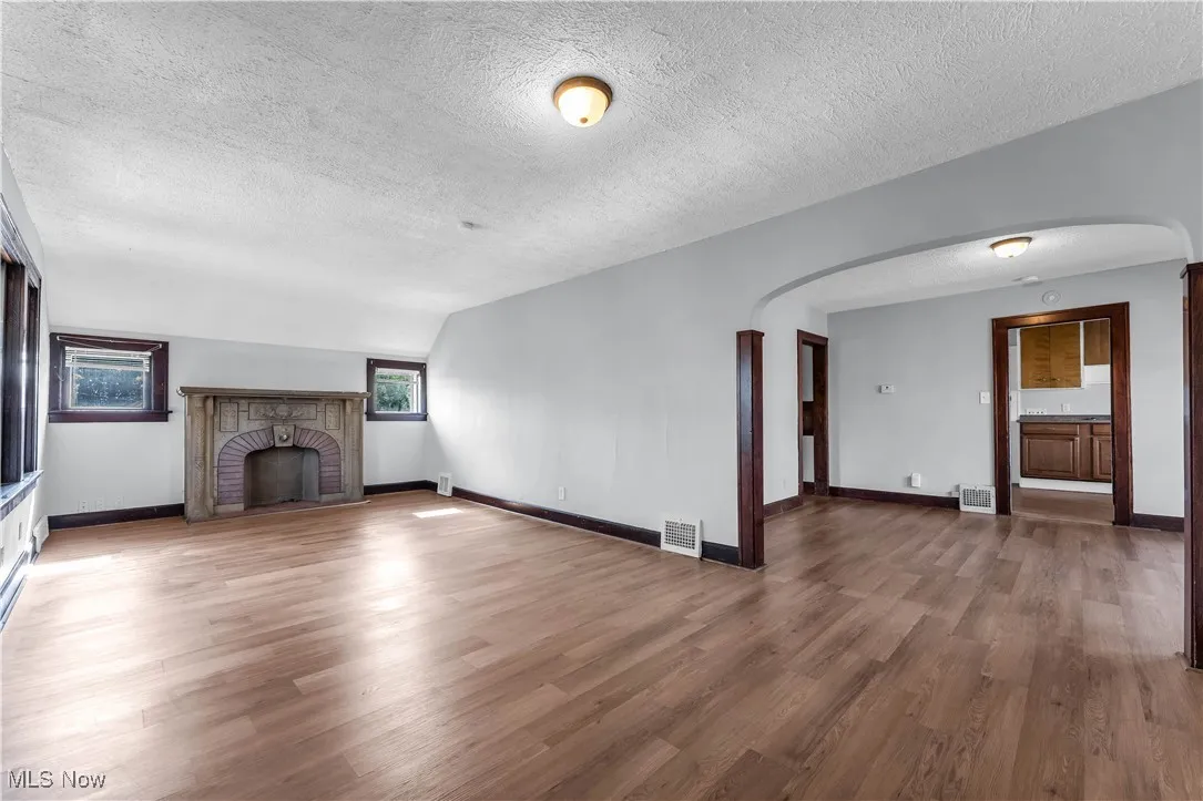 Unfurnished living room featuring a textured ceiling, wood finished floors, a brick fireplace, and arched walkways