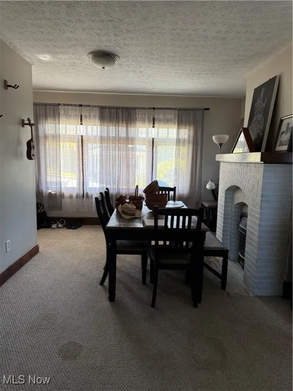 Carpeted dining area with a textured ceiling and a brick fireplace