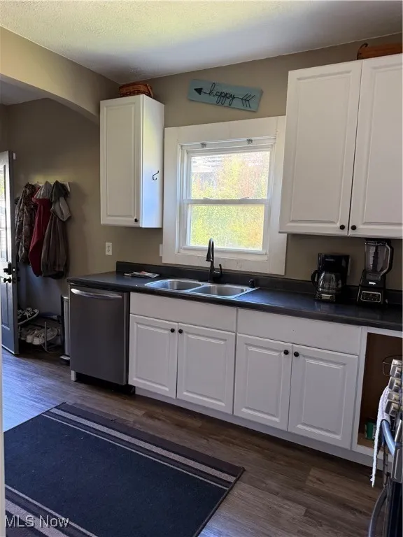 Kitchen with dark countertops, white cabinets, dark wood-style floors, dishwasher, and a textured ceiling