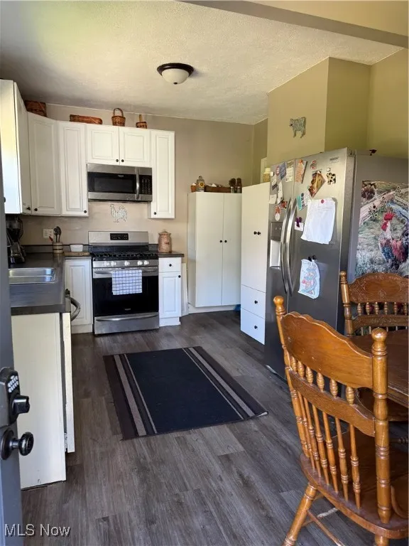Kitchen with dark countertops, white cabinets, white stove, black fridge, and a textured ceiling