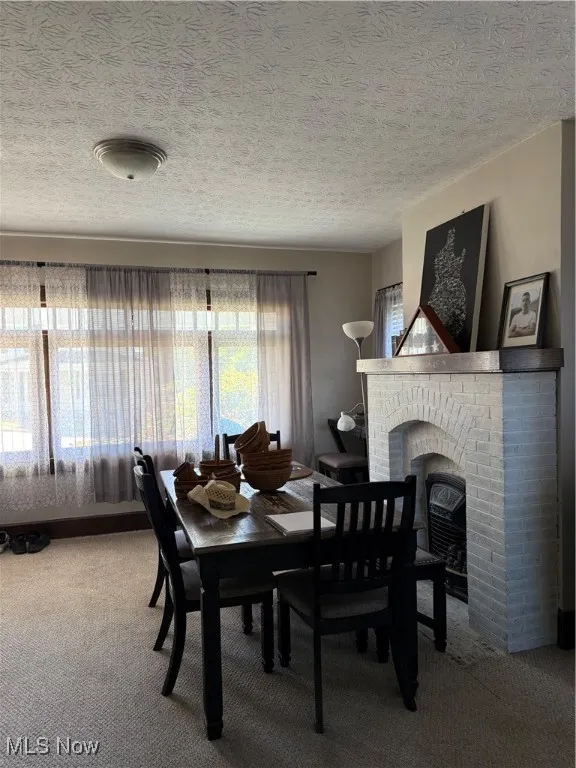 Dining area with plenty of natural light, a fireplace, carpet flooring, and a textured ceiling