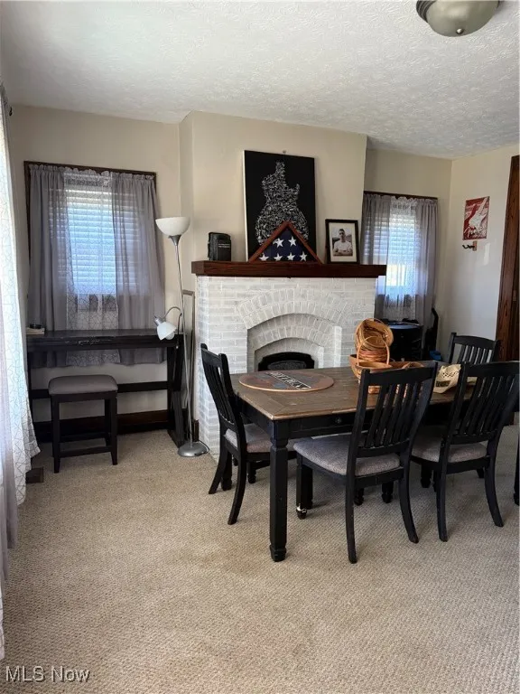 Dining area with a fireplace, a textured ceiling, and light colored carpet