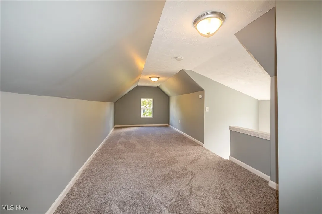 Additional living space featuring light carpet, vaulted ceiling, and a textured ceiling