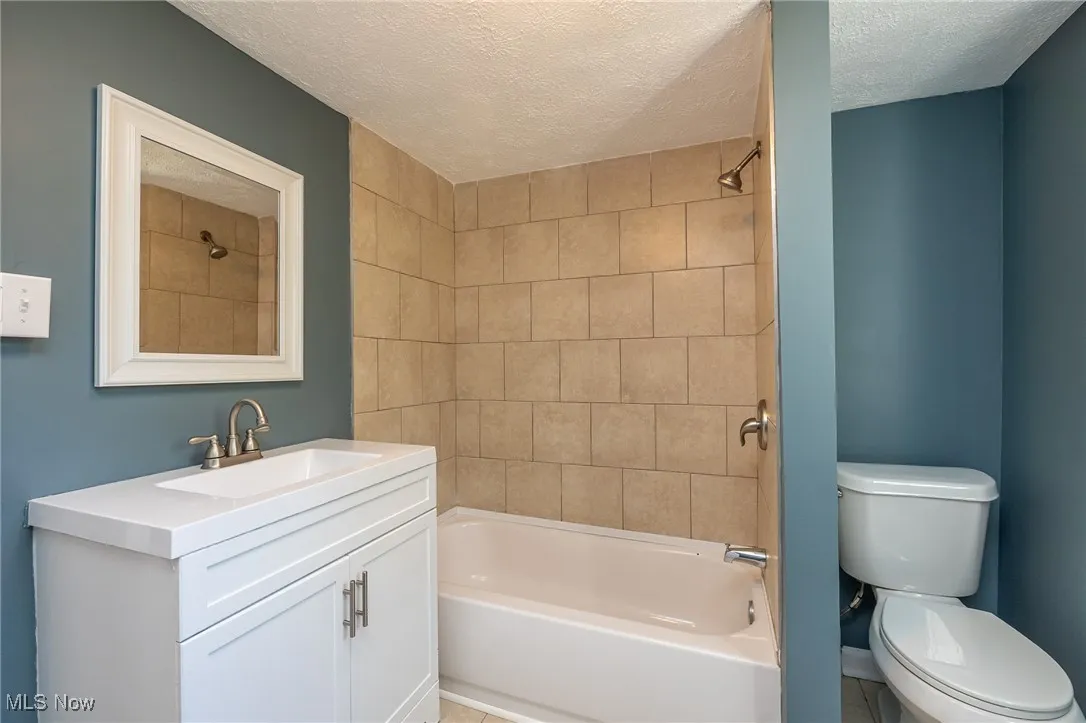 Bathroom featuring tub / shower combination, a textured ceiling, vanity, and light tile patterned flooring